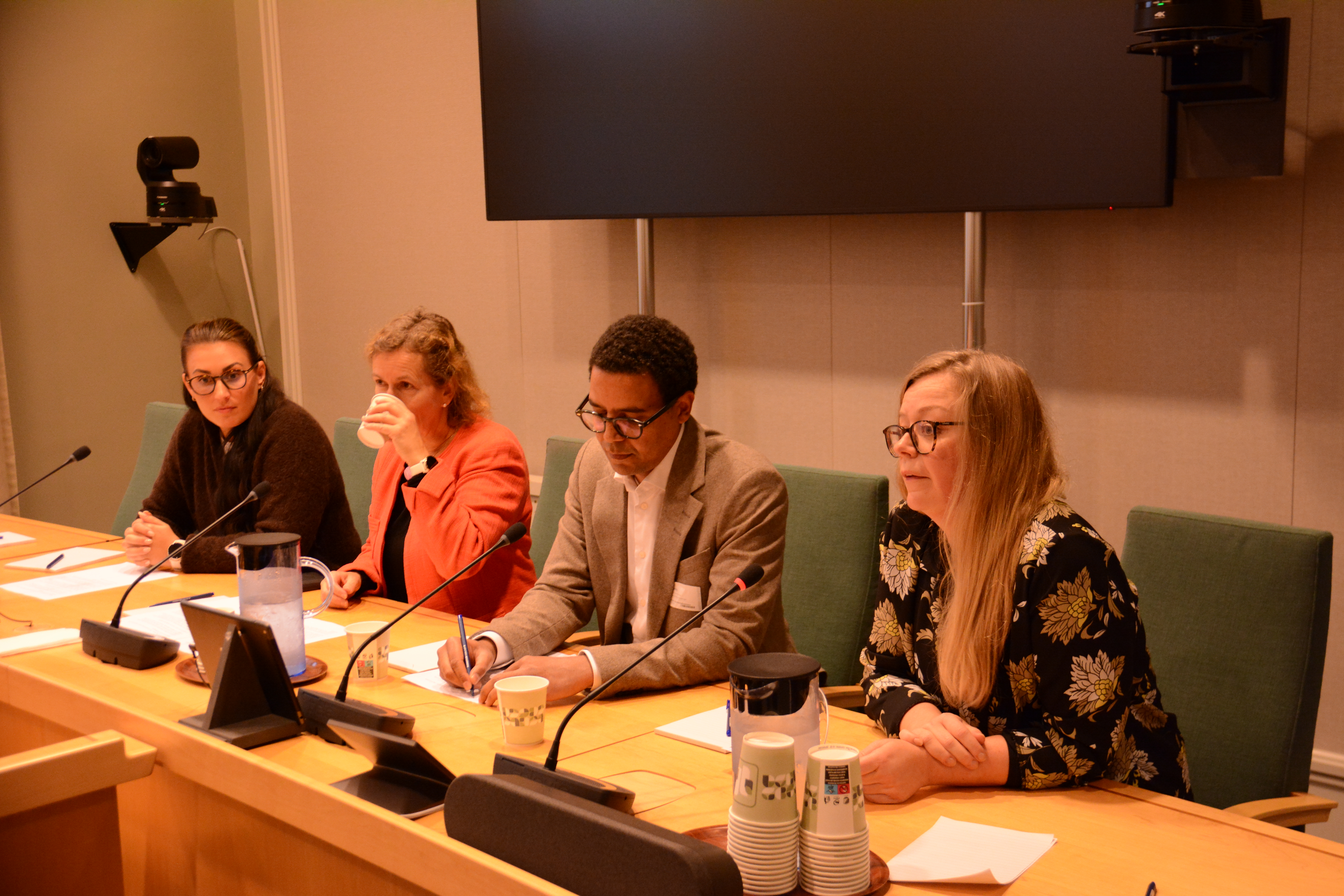 Fire personer sitter bak et bord med mikrofoner